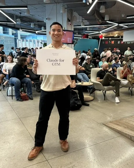 A facilitator holding a 'Claude for GTM' sign in front of a seated crowd