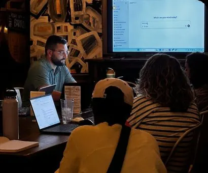 A coach at a laptop with attendees leaning in to watch