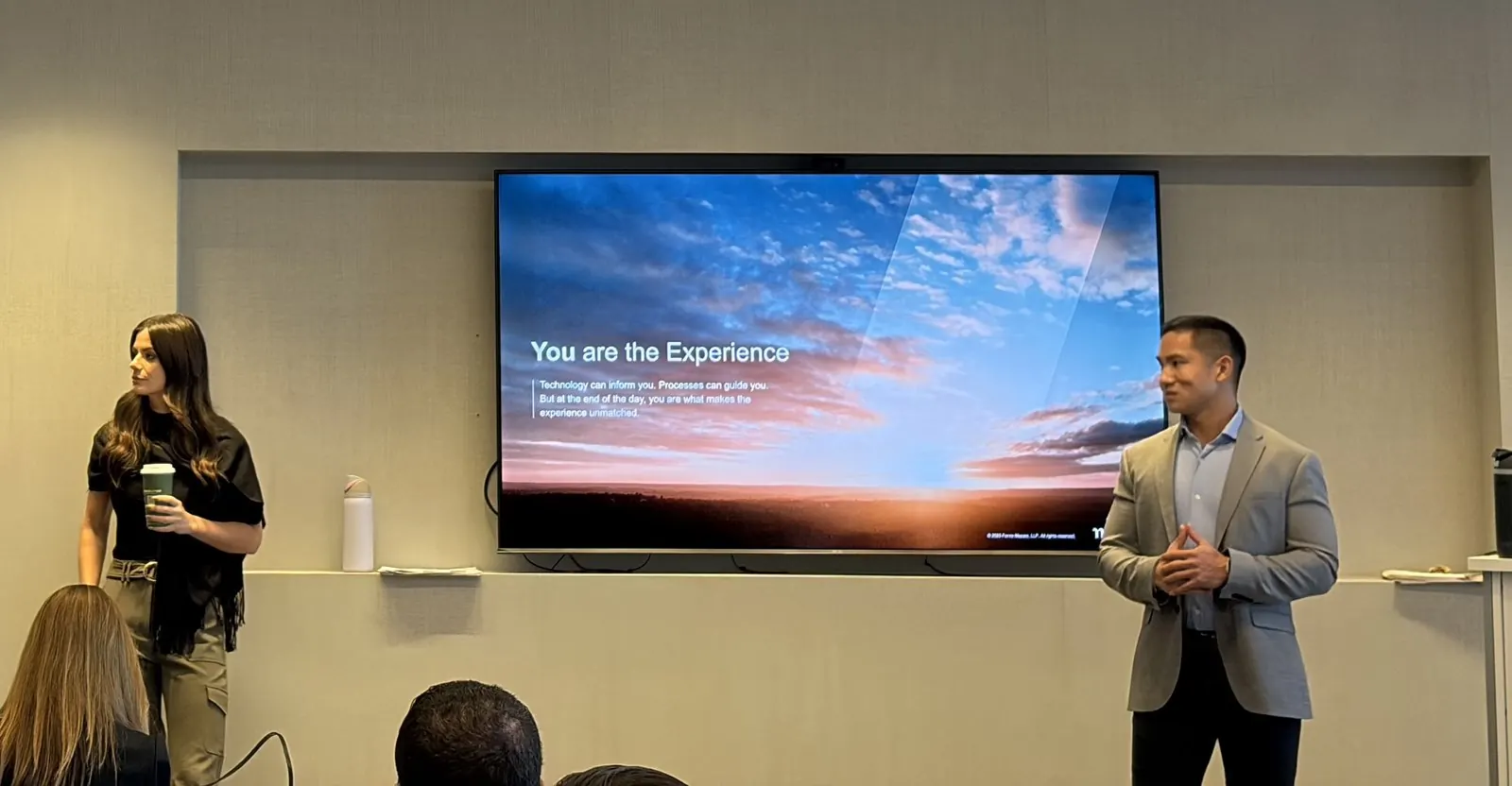 A facilitator speaking next to a screen that reads 'You are the Experience'